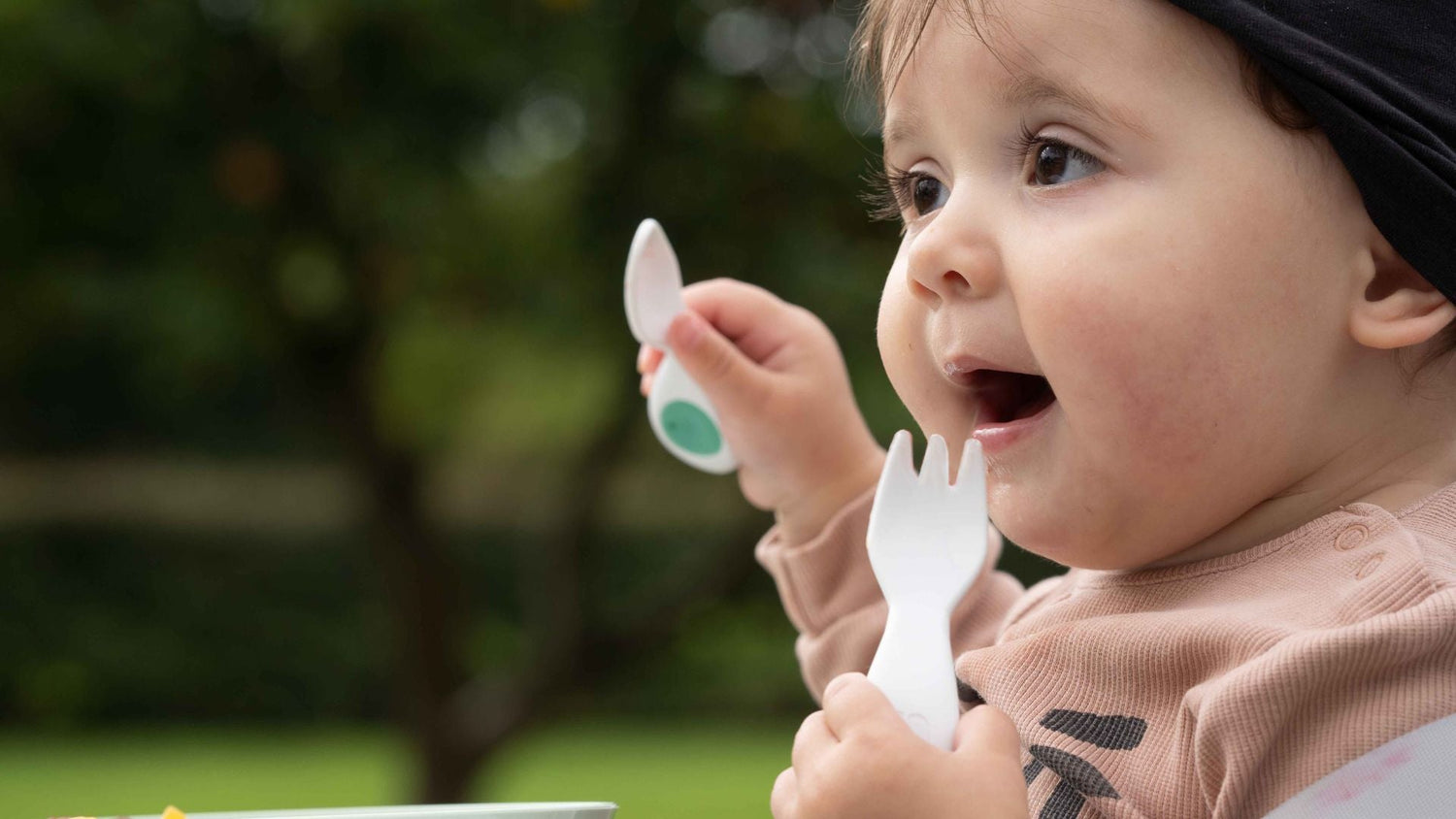 Happy baby holding a doddl baby fork and spoon
