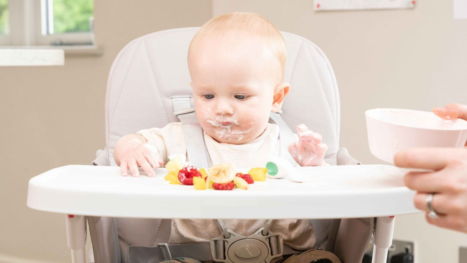 Baby sitting in highchair with finger foods of fruit in the tray in front of him