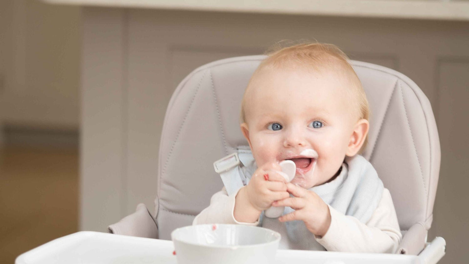 Happy baby sitting in highchair eating food with a doddl spoon
