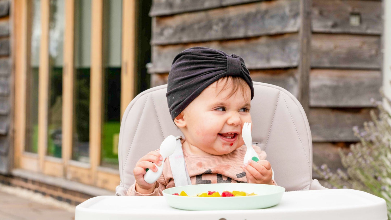 Happy toddler girl sits in a highchair in the garden with fruit as a snack