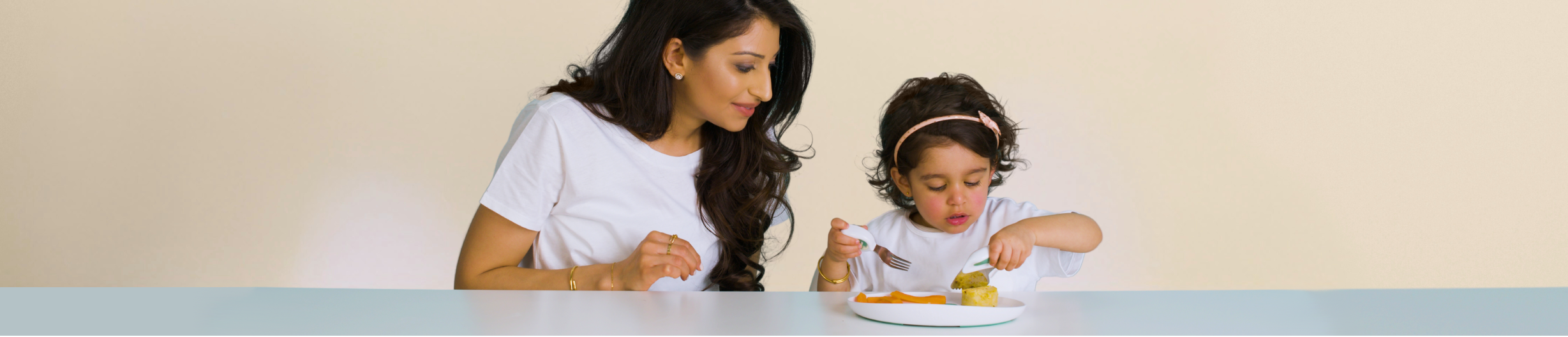 Woman and child sitting at a table with doddl plate and doddl toddler cutlery against a beige background