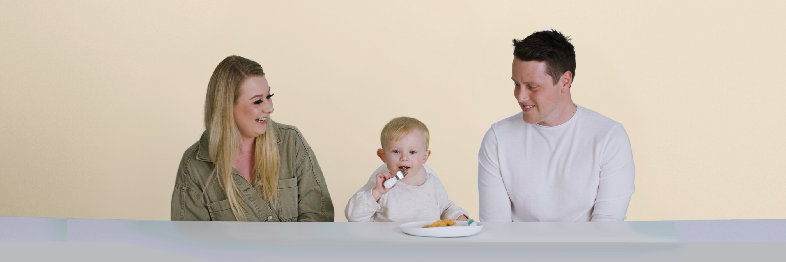 Two adults and a child using doddl plate and toddler cutlery sitting at a table with a plain background